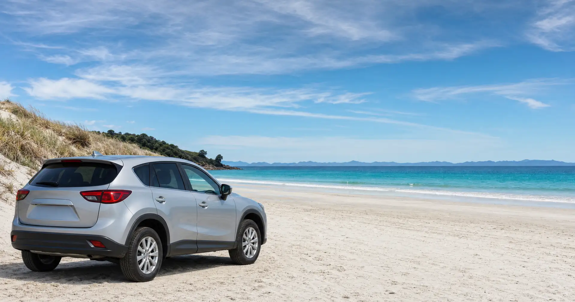 A compact SUV parked on firm sand at the edge of a white sand beach