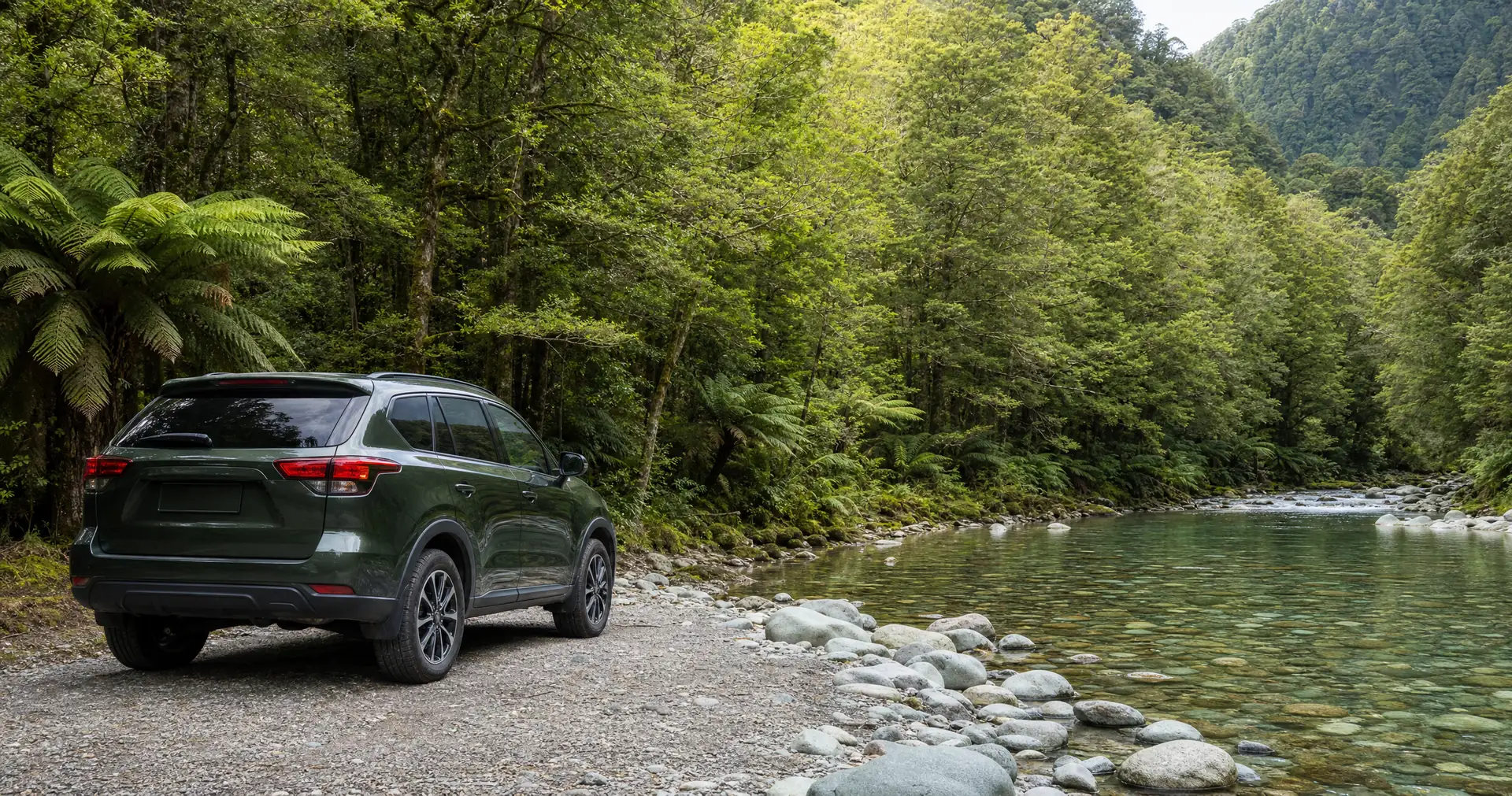 A compact SUV parked on a gravel road beside a clear river in a bush valley